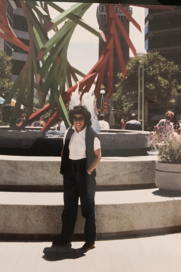 Gigi in a white shirt and black waistcoat, standing in front of Roselyn Mazzilli's sculpture THERE! at Oakland City Center.