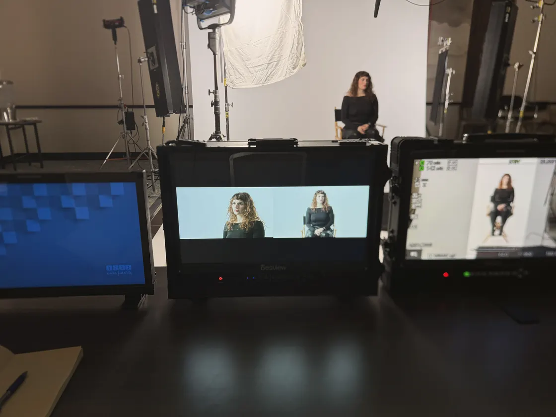 A studio set at the Summit: two people on camera, three monitors showing the feed, lights and flags around them.