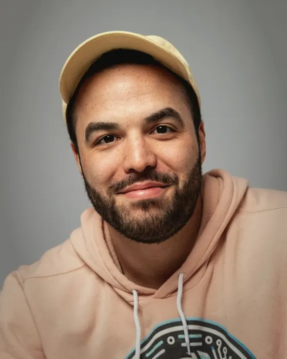 Portrait one: me in a pink hoodie and a yellow cap, sitting against a plain grey backdrop.